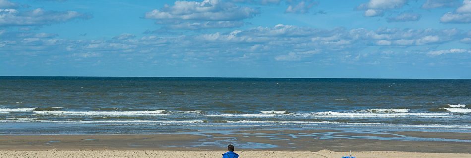 man-in-blue-jacket-in-a-beach-near-blue-trash-bins