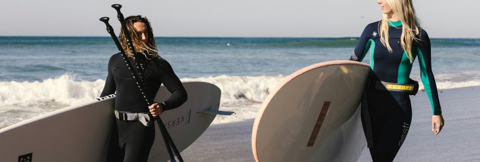 two-women-in-wetsuits-carrying-surfboards-on-the-beach