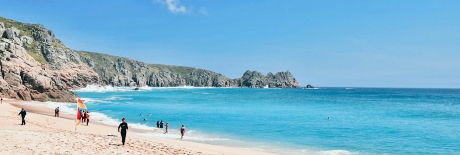 Porthcurno - a group of people standing on top of a sandy beach