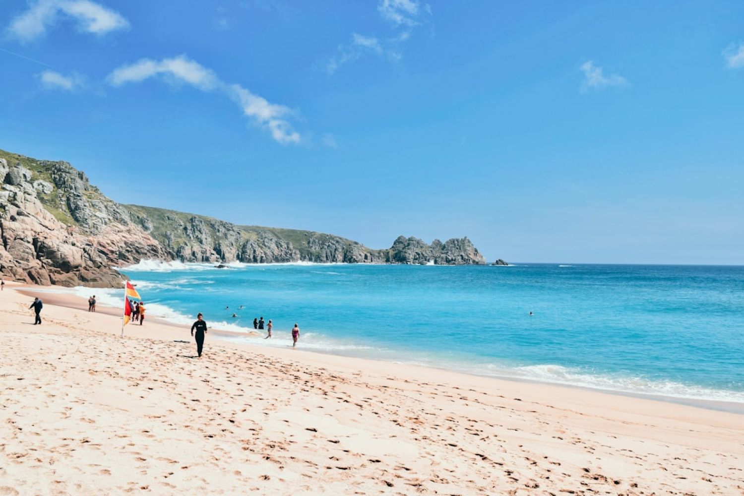 Porthcurno - a group of people standing on top of a sandy beach