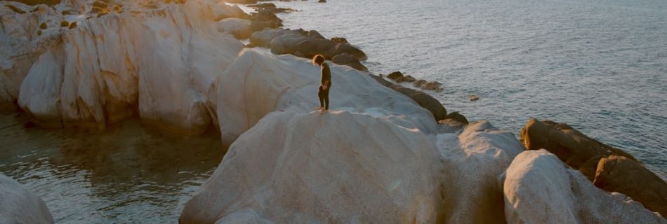 Coastal - photo of person standing on brown boulder surrounded by water