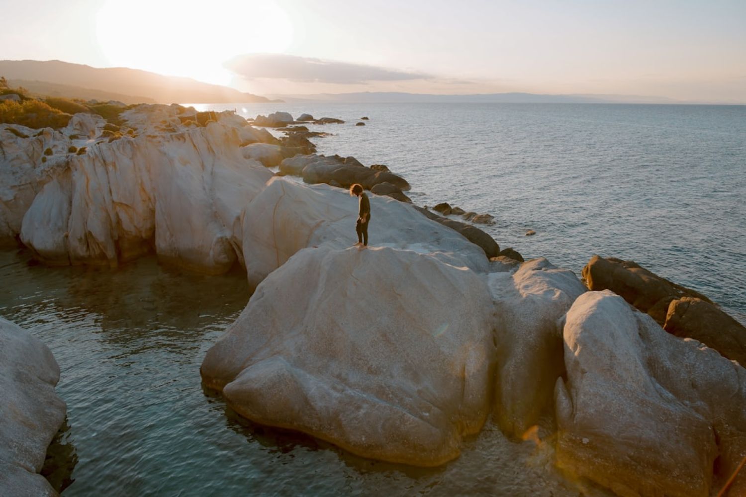 Coastal - photo of person standing on brown boulder surrounded by water